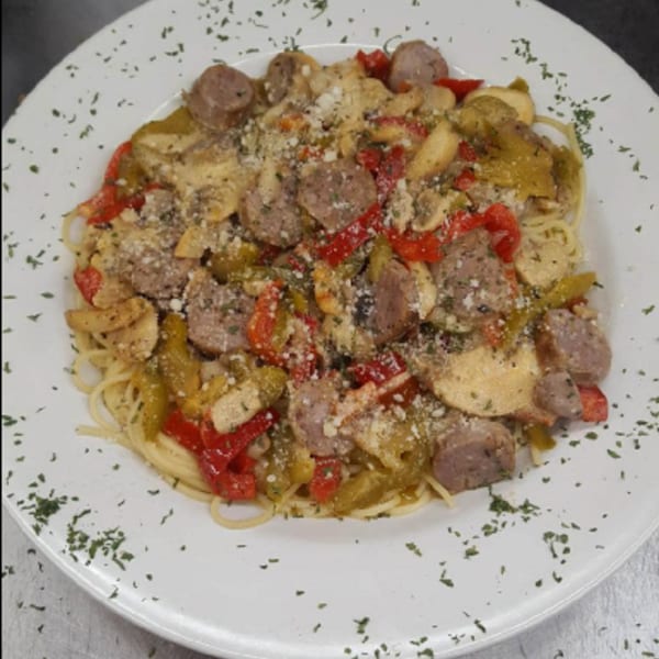 Spaghetti with sliced sausage, red and green peppers, and grated cheese on a white plate.