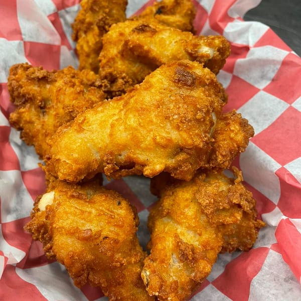 Crispy golden-brown chicken wings in a red and white checkered paper-lined basket.