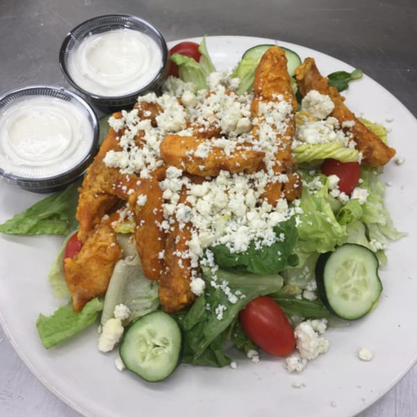 A buffalo chicken salad with lettuce, tomatoes, cucumbers, blue cheese crumbles, and two ranch cups.