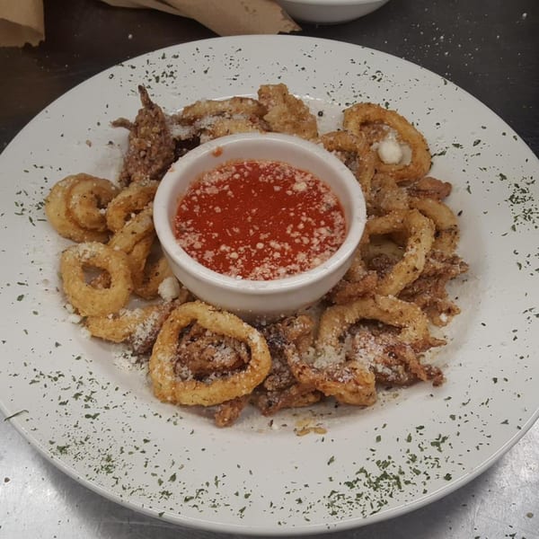 Crispy fried calamari rings and tentacles with a side of marinara sauce, garnished with parsley and parmesan.