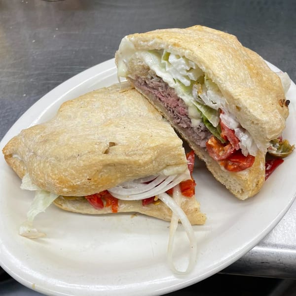 Two halves of a Yetty's Pizza sandwich with meat, cheese, lettuce, onions, and red peppers.