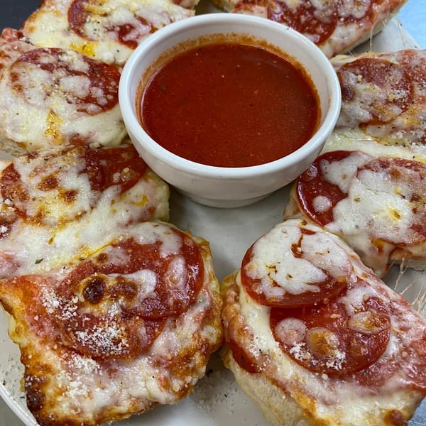 Pepperoni pizza slices with melted cheese and a side of red dipping sauce from Yetty's Pizza.