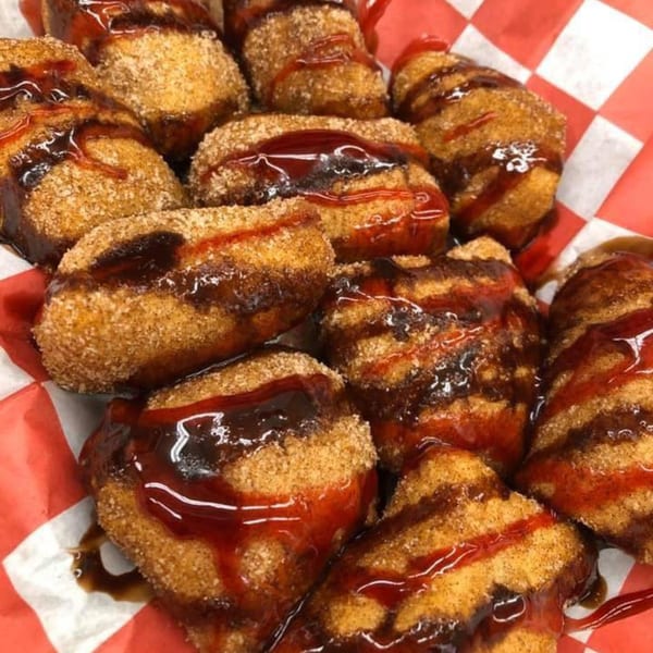 Close-up of golden-brown churro bites drizzled with chocolate and strawberry syrup in a red and white checkered basket.
