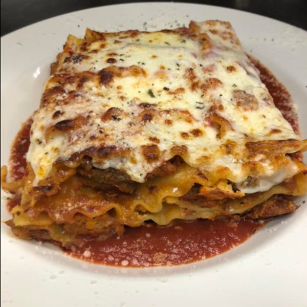 A large, cheesy slice of lasagna with rich red sauce on a white plate.