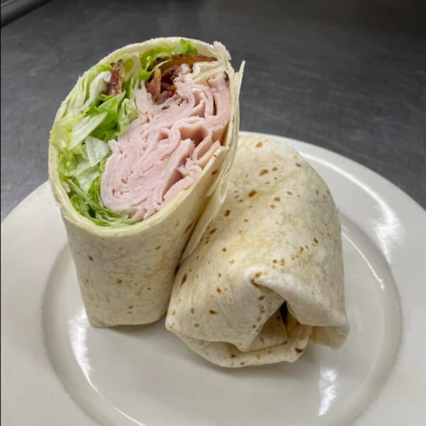 Two turkey and bacon wraps with lettuce, one cut in half, on a white plate.